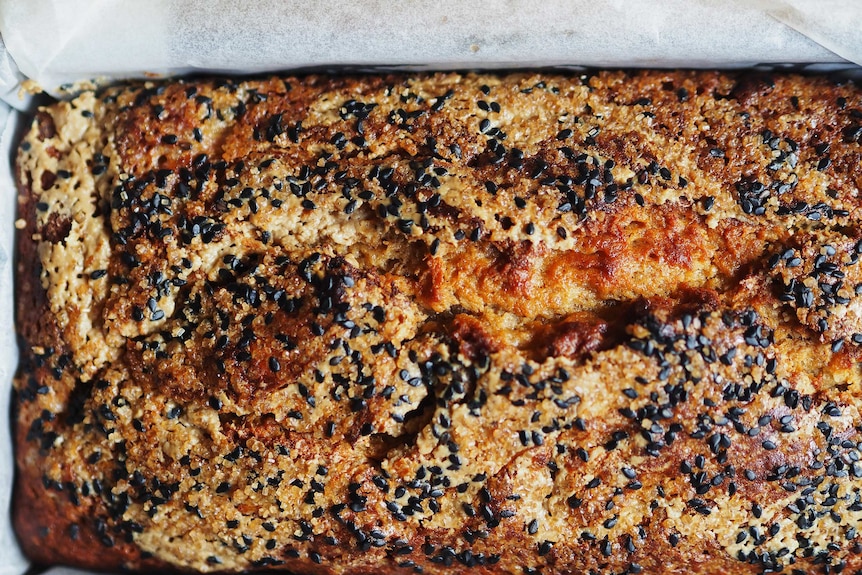 A close up of a freshly baked banana bread topped with tahini, raw sugar, black sesame seeds, an easy and warming bake.