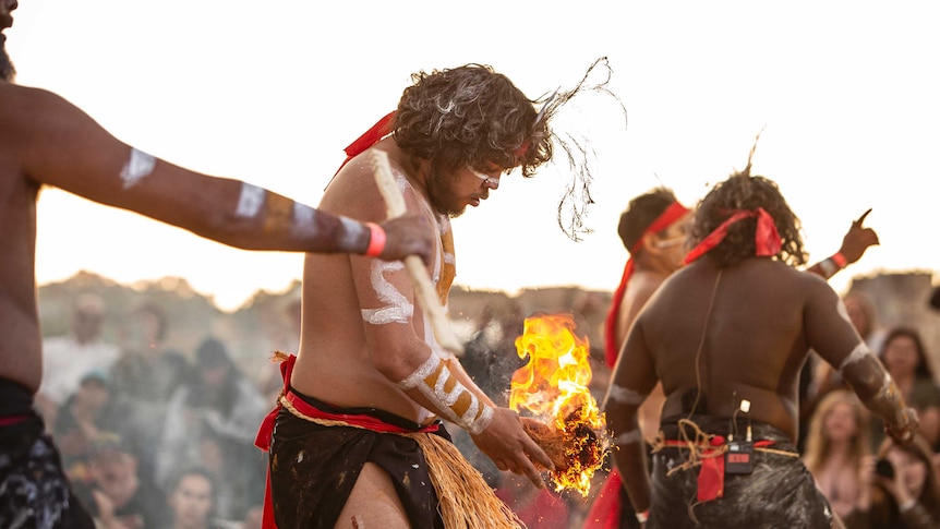 Colour side on photo of Ashley Ruska of dance group Nunukul Yuggera holding small fire during performance at Dance Rites 2018.