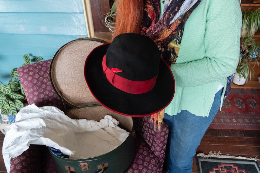 A woman holds a black felt hat with a red band and trim.