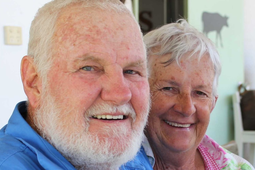 A man with his arm around a woman on a bench outside their home.