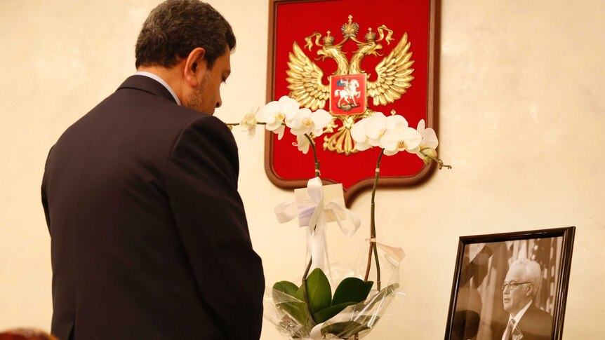A man stands in front of flowers and a picture of the late Vitaly Churkin, Russia's ambassador to the UN.