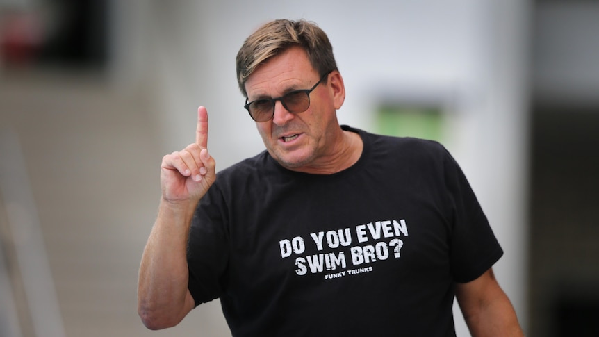 A man wearing sunglasses and a shirt saying "Do you even swim bro?" pointing his finger in the air 