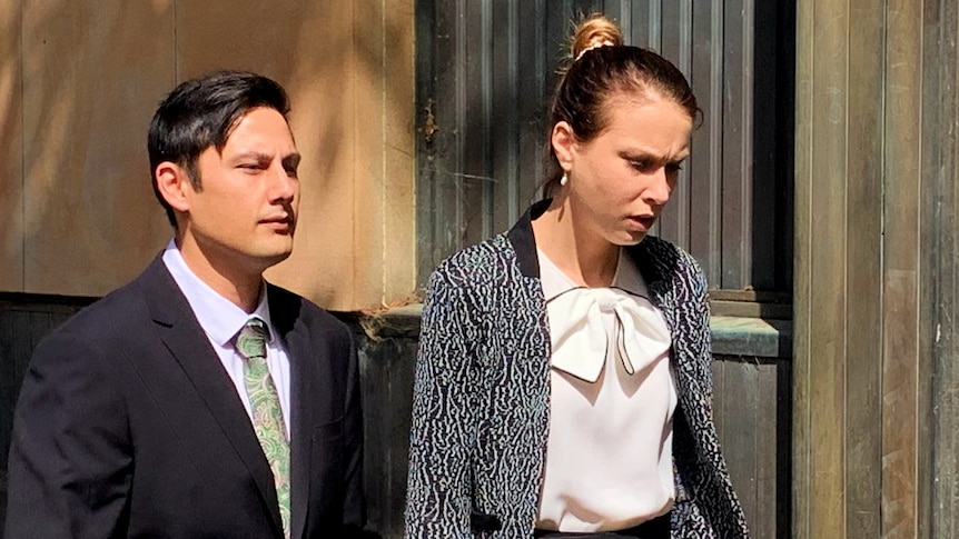 A man and woman walk along a street holding hands.