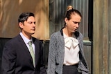 A man and woman walk along a street holding hands.