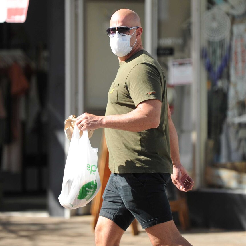 A man wears a white mask over his mouth and nose while carrying a shopping bag.