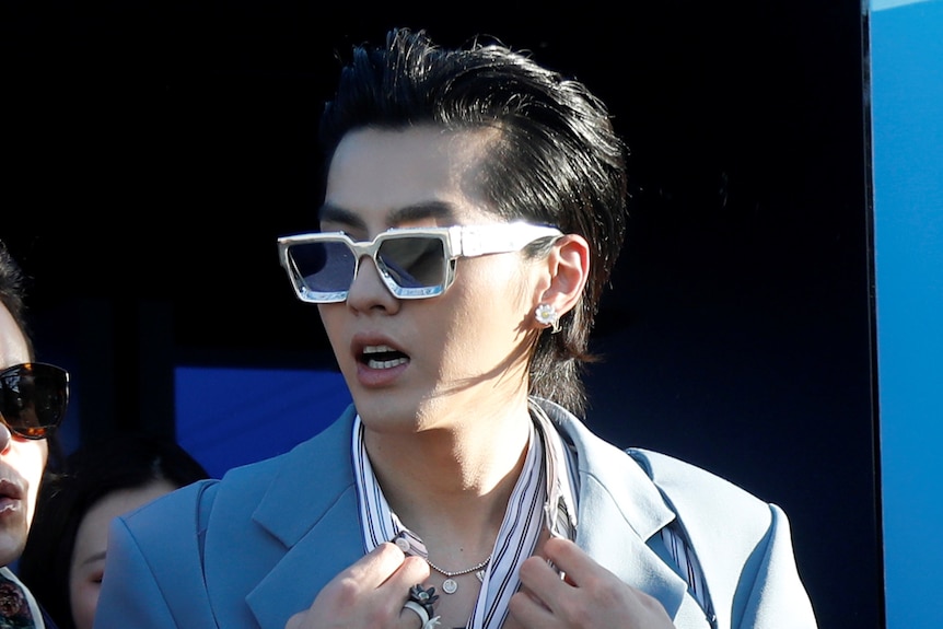 Kris Wu dans un costume bleu pâle et des lunettes de soleil, agrippant ses revers 