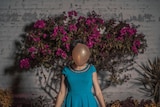 A woman stands in front of a flowering plant, but her face is hidden behind a floating balloon.