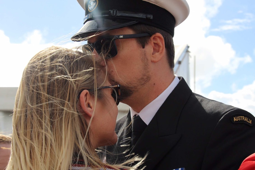 Man in full navy uniform kisses the forehead of his fiance.