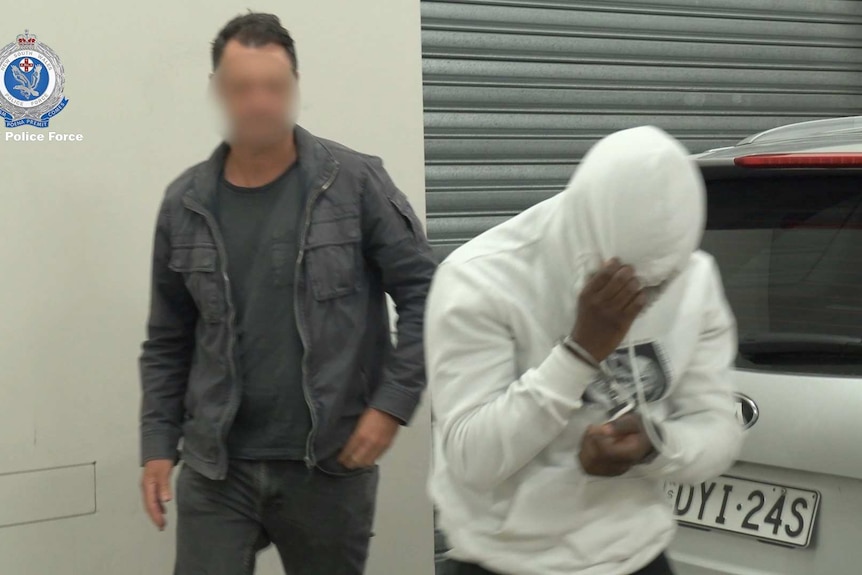 A man with a hoodie on hides his face from the camera