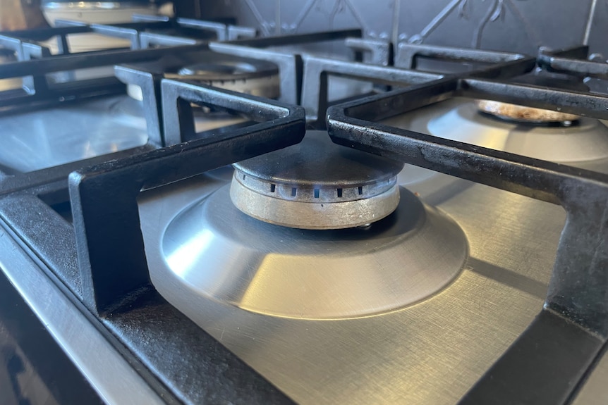 A faint blue flame is burning from a gas element on a stainless steel cooktop