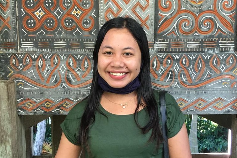 A woman standing in front of a wall of art smiling to camera.