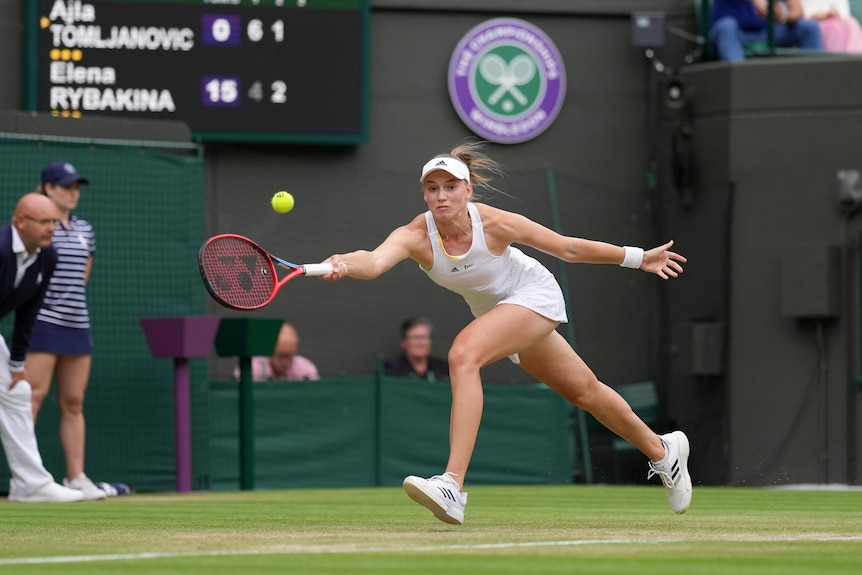 A woman in white stretching for a tennis ball on a grass court at Wimbledon