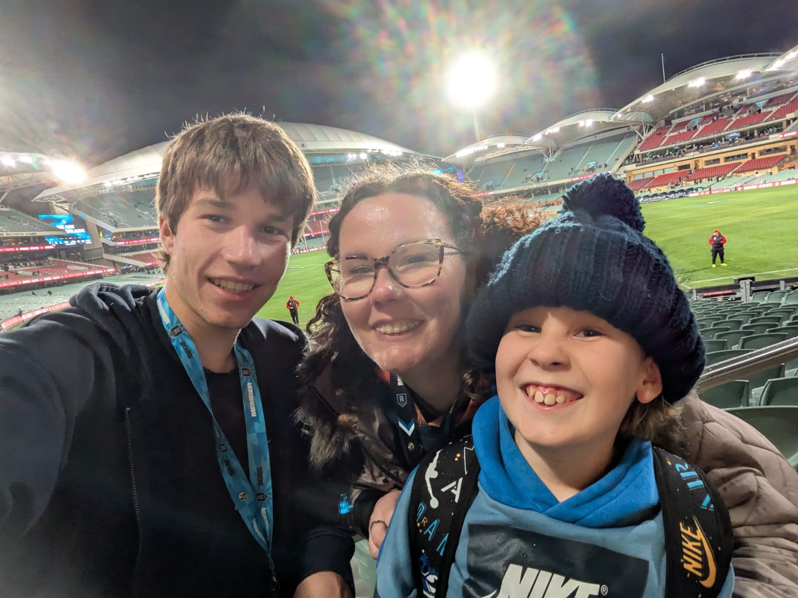 a young man takes a selfie next to a woman hugging her son, oval seats in the background