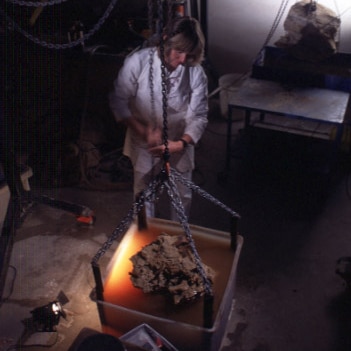 A woman in a dark room stands above a rock she's about to dip a bucket.