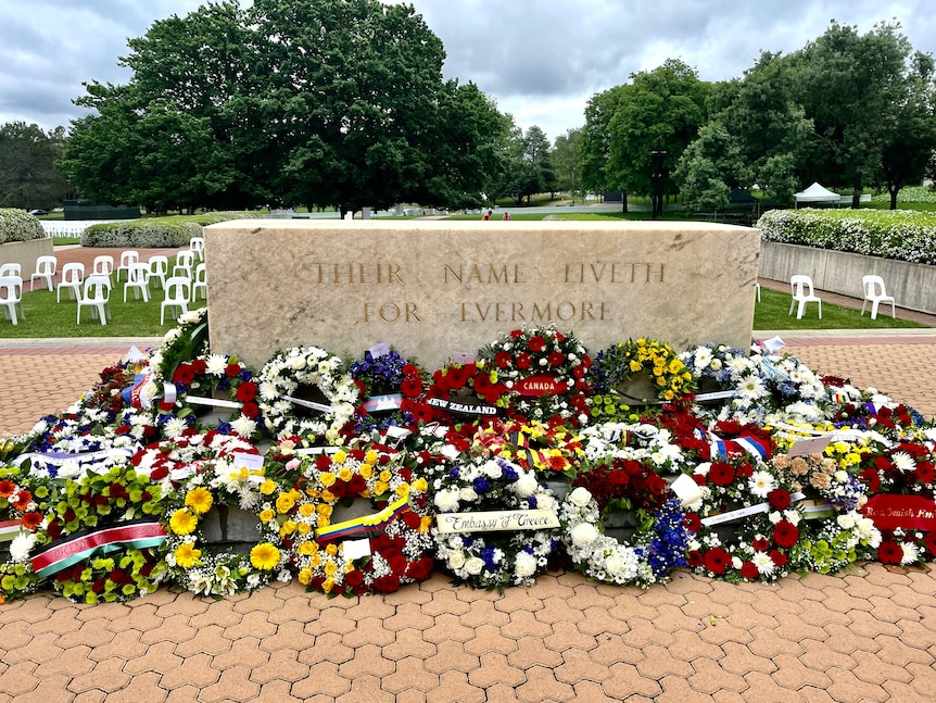 The memorial stone has wreathes laid against it.