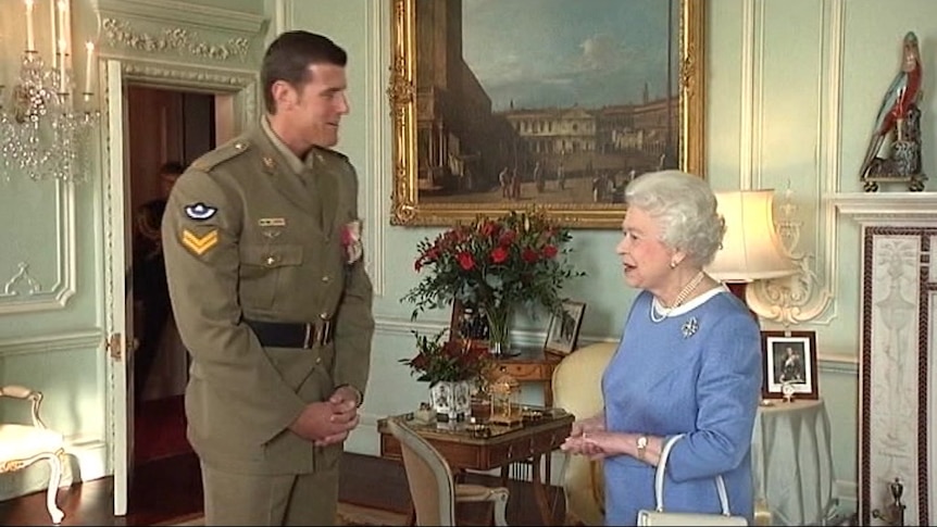 A tall man in military uniform speaks with Queen Elizabeth in an ornate room