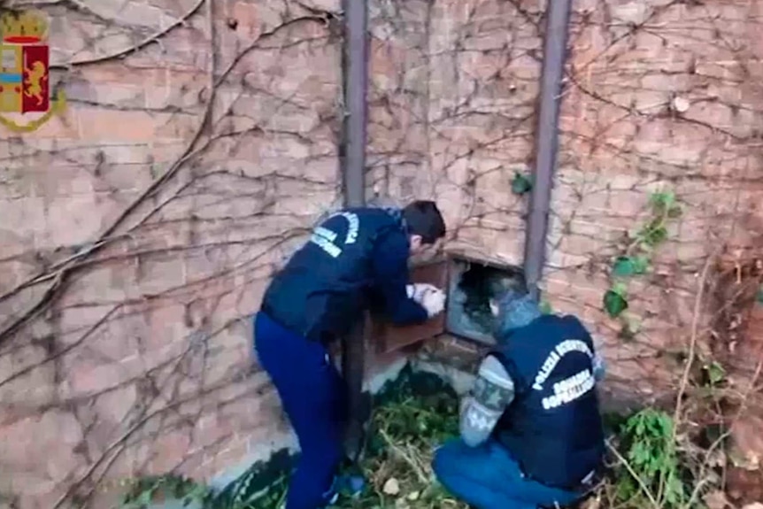 Two forensic police officers look closely inside the hidden trap door