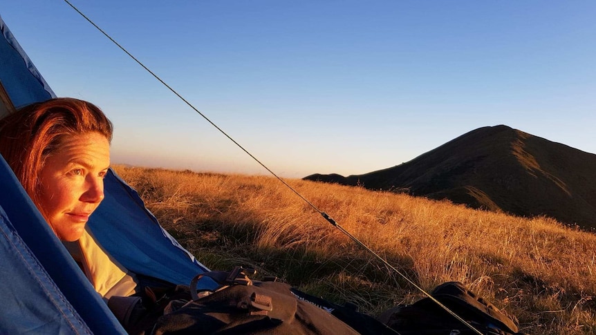 Woman stares out of a small blue tent in high country at dusk