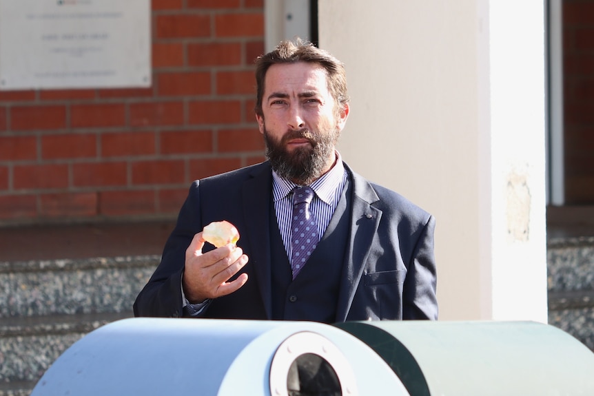 Bearded man wearing suit eats apple in front of retro court building.