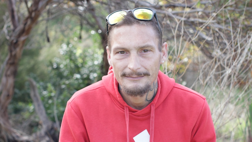 A man with a red hoodie and sunglasses on the top of his head looks at the camera.