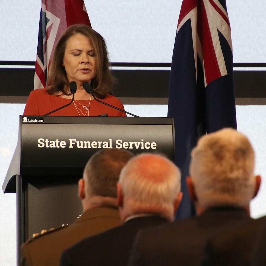A wide shot of Kim Farmer delivering the opening eulogy at a state funeral for Graham "Polly" Farmer.