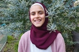 A smiling teen wearing a hijab in front of greenery