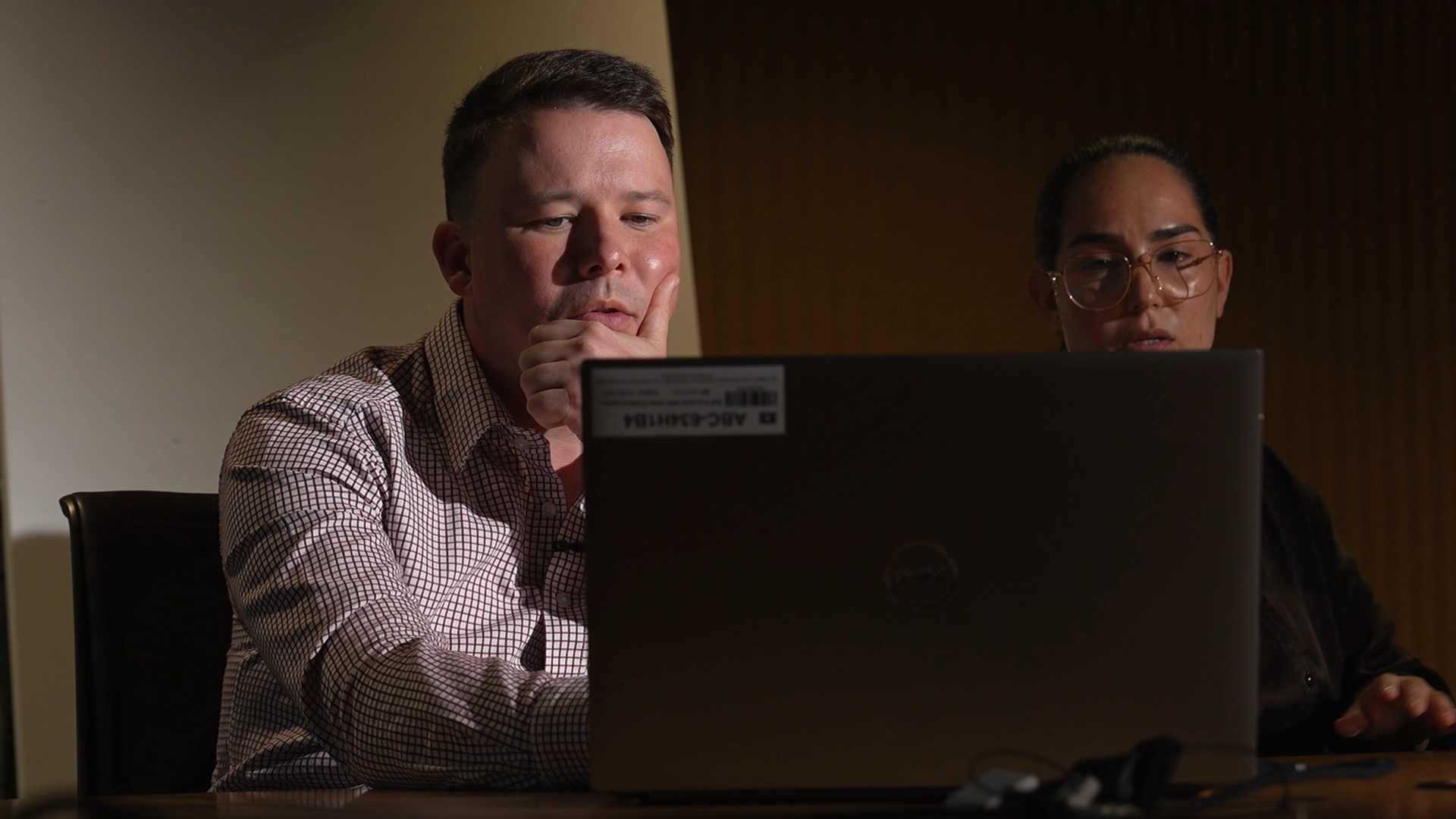 A man and a woman look over a laptop computer as their faces glow from the screen
