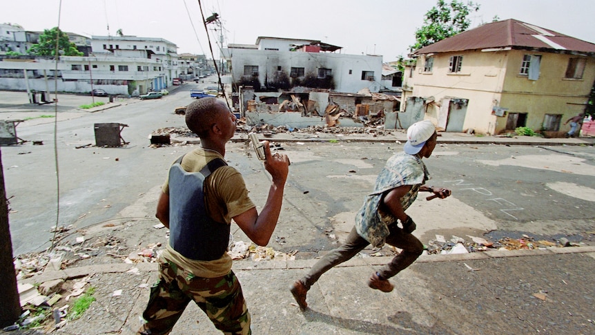 Two militiamen of Charles Taylor's National Patriotic Front of Liberia (NPFL) run, armed with guns