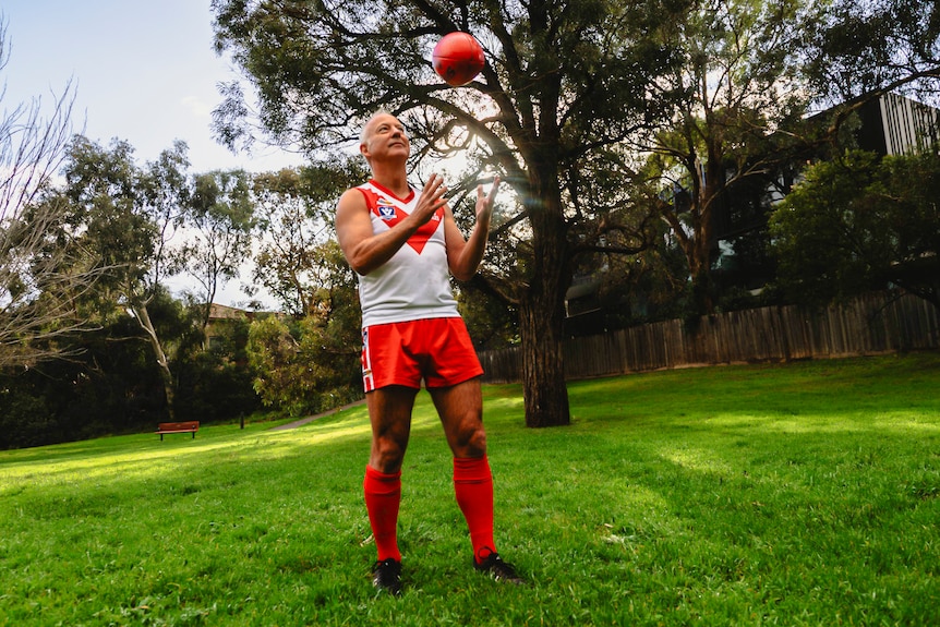 A man wearing an Aussie Rules uniform juggles a football.