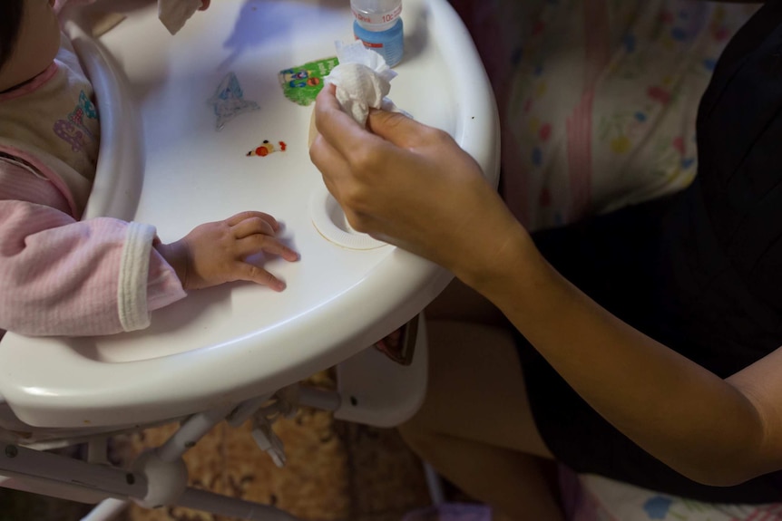 A close up of Layla's hand, holding a scrunched up paper towel as she prepares to wipe Tia's hands, as she sits in a high chair