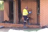 A firefighter writing on a pad while standing outside a burnt house with broken windows and soot covered walls