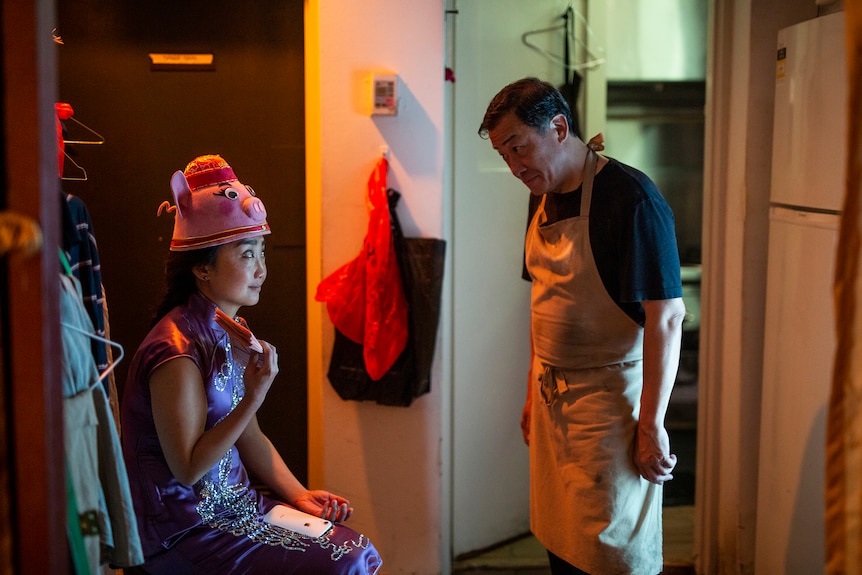 Chinese Australia woman in purple kimono and pig hat looks cheekily at Chinese man wearing apron.