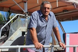 A man with grey hair, wearing a blue shirt, standing on the deck of a boat.