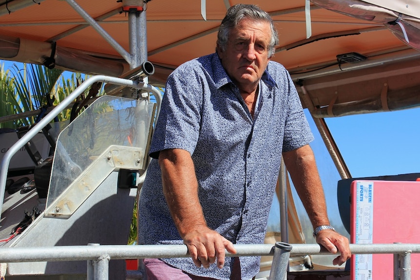 A man with grey hair, wearing a blue shirt, standing on the deck of a boat.