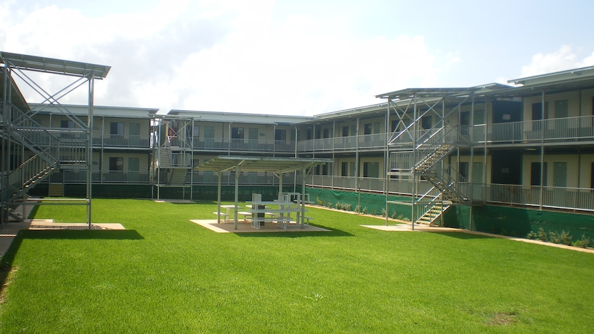 A two-storey building wraps around three sides of a large green grass quadrangle.  