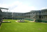 A two-storey building wraps around three sides of a large green grass quadrangle.  