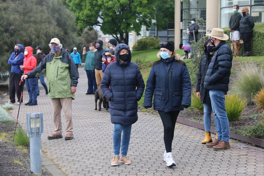 People wearing masks stand around and look out to sea.