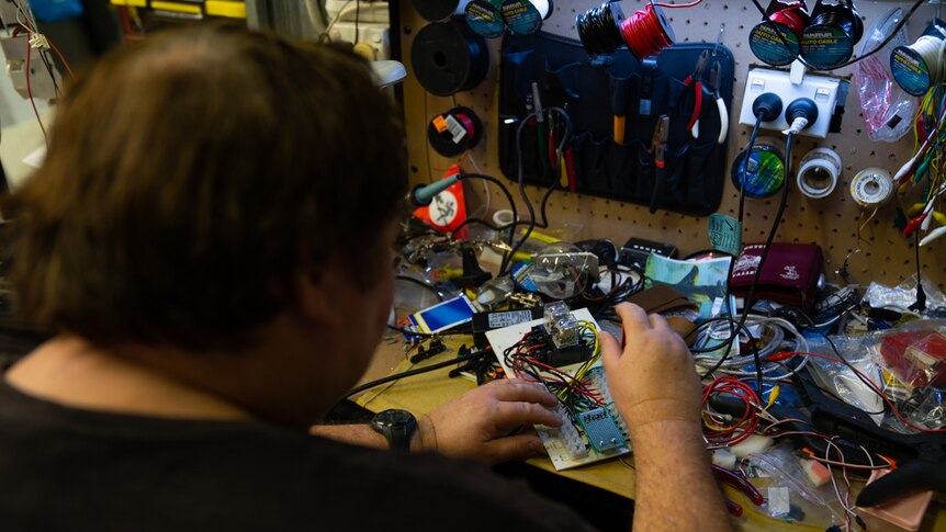 Robot maker Paul Aitken plays with a circuit board at his workshop bench.