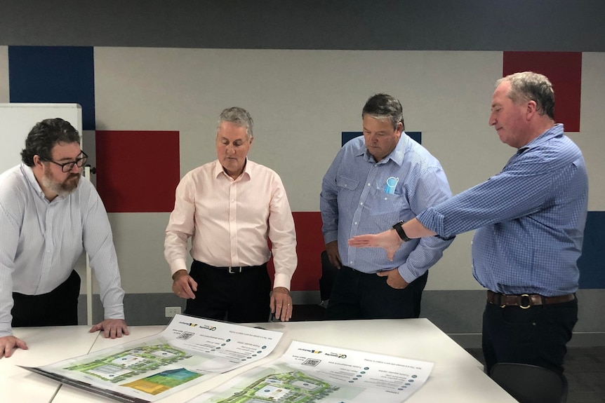 Four men stand around a table looking at a some plans