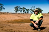 Drought-affected farmer Graham Nesbit on the edge of an empty dam with sheep in the background