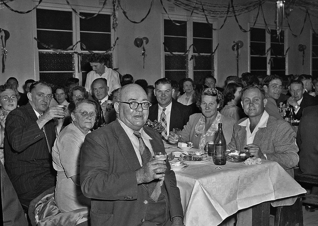 A black and white photograph of people drinking and eating in a decorated hall