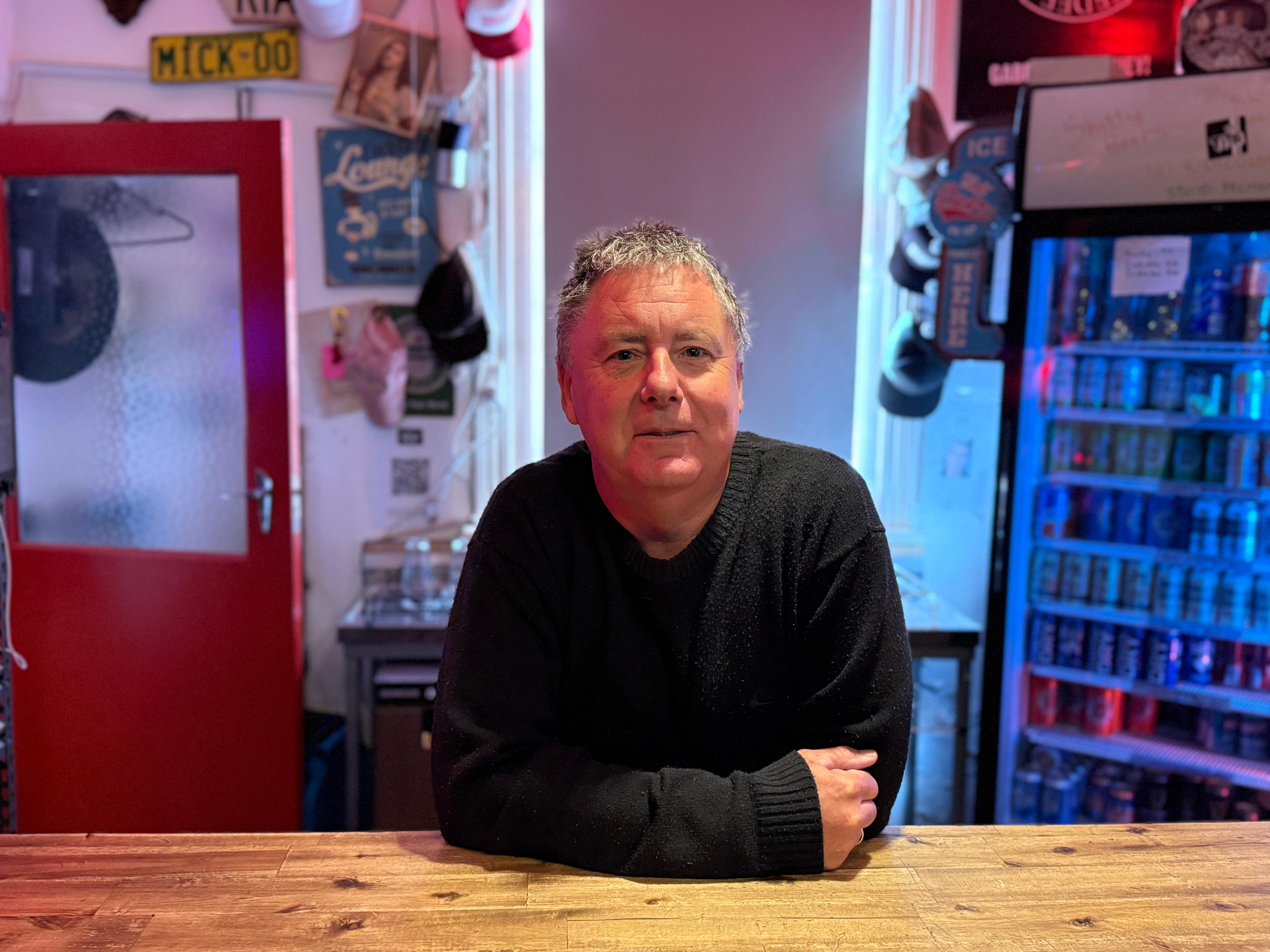 Um homem está atrás de um bar com os braços cruzados sobre a mesa.
