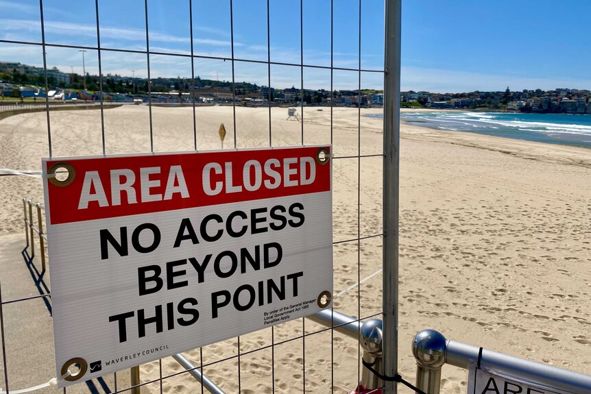 A sign that reads "Area Closed No Access Beyond This Point" with a deserted beach in the background
