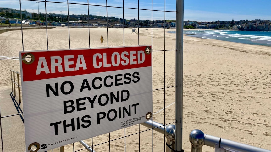 A sign that reads "Area Closed No Access Beyond This Point" with a deserted beach in the background