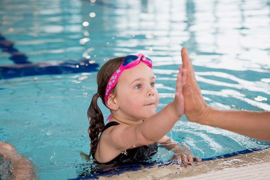 A little girl in a pool high-fives an adult.