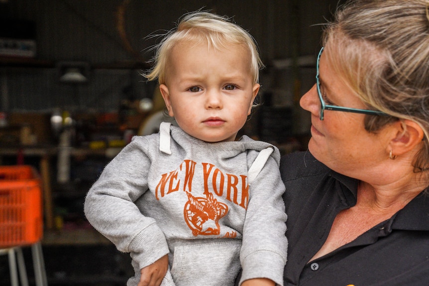 A woman wearing a polo shirt holds a young blonde-haired toddler.