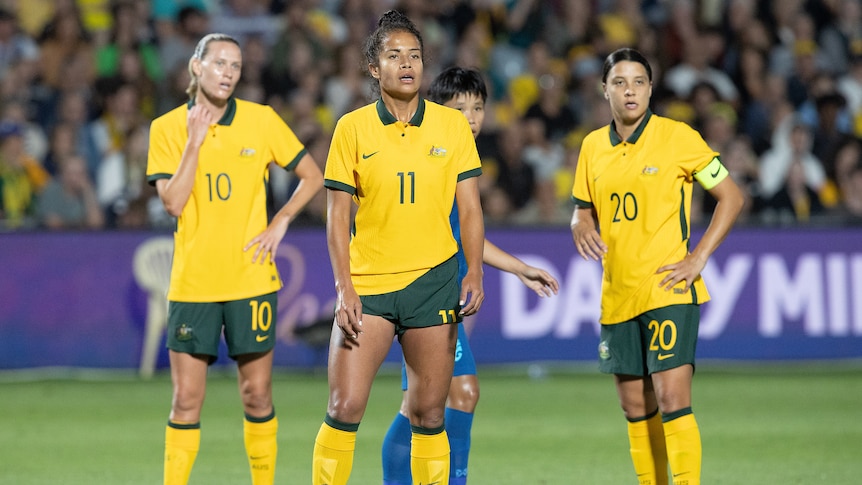 Matildas players Emily van Egmond, Mary Fowler and Sam Kerr stand on a football field waiting for a corner.