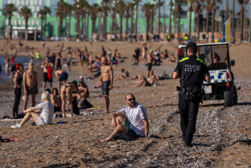 A uniformed officer walks through a crowd of people enjoying the beach