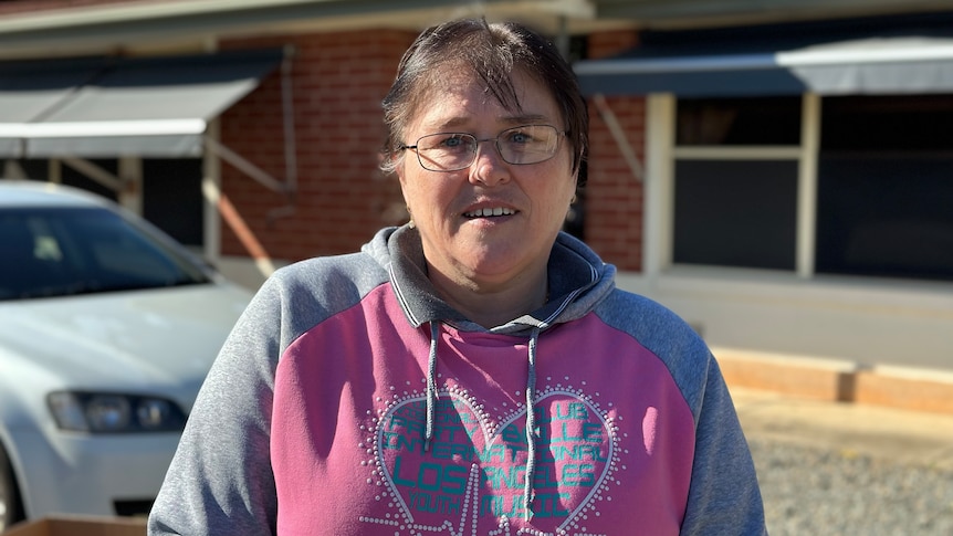 A woman standing out the front of her home smiling at the camera