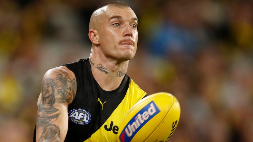 A Richmond Tigers AFL player handballs with his right hand. 